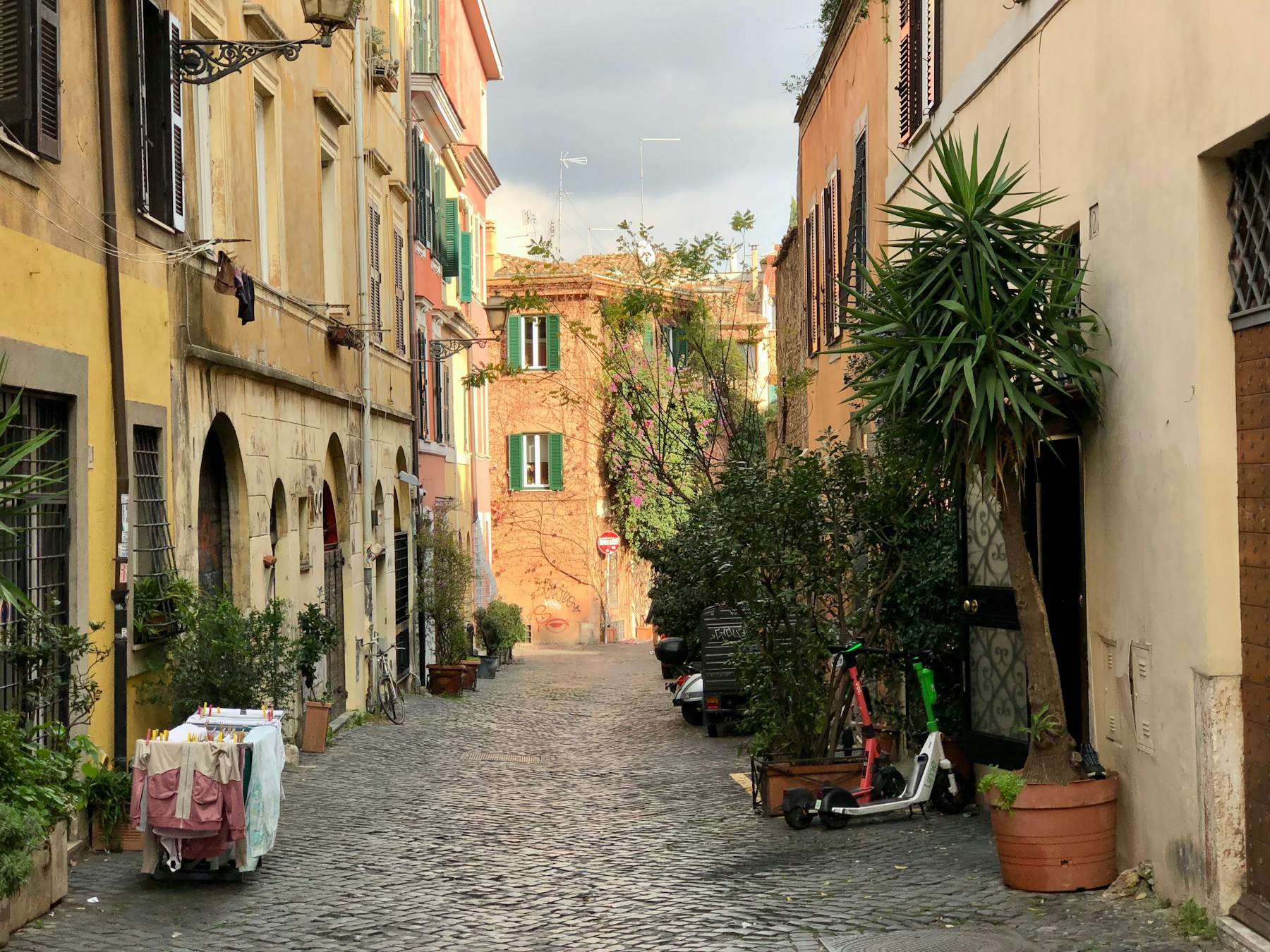 A cobblestone lane with colorful buildings and greenery in Trastevere, Rome